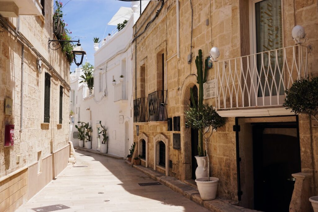 Sunny narrow alley in Bari lined with white and stone buildings.