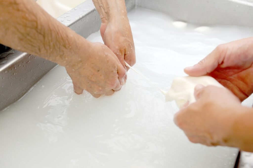 mains façonnant mozzarella dans une bassine d'eau laiteuse à Bari