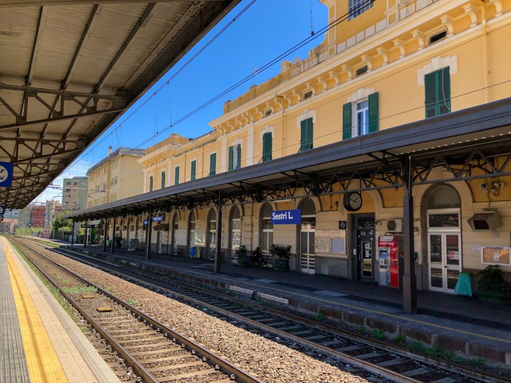 Banchina ferroviaria con binari e l'edificio giallo della stazione Sestri L.