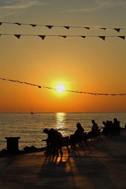 Tramonto sul mare a Bari con persone in controluce sulla banchina