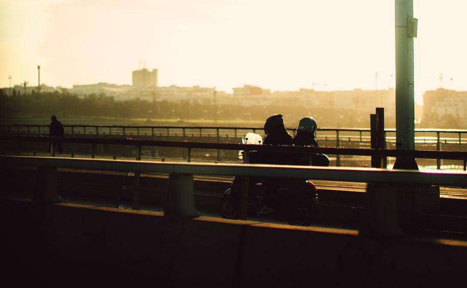 Zwei Personen als Silhouetten auf einem Roller auf Brücke bei Sonnenuntergang in Bari