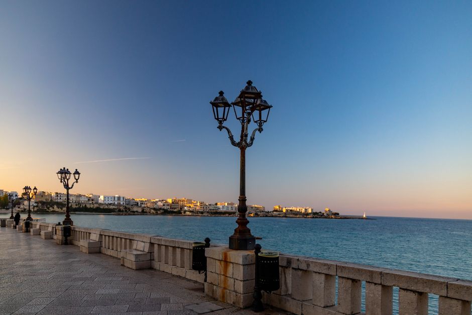 Bari seaside promenade at sunset with lampposts and distant lighthouse