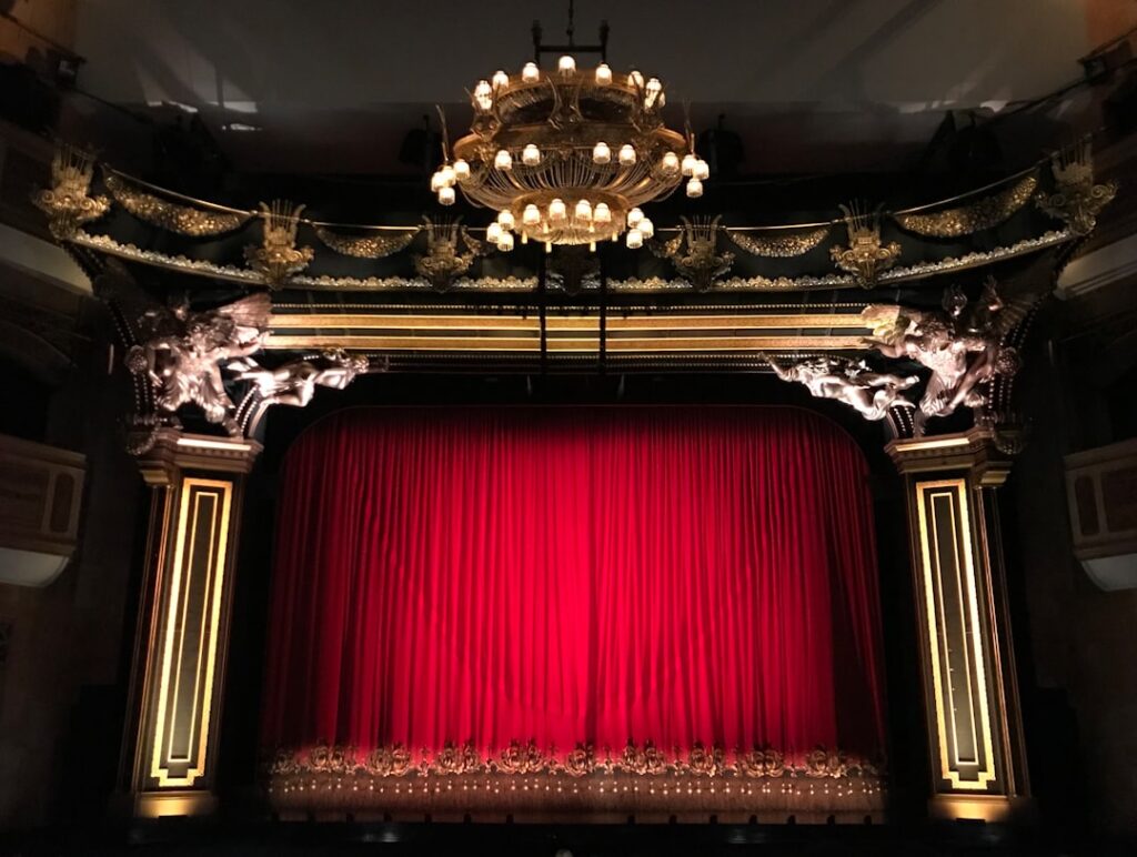Red stage curtain framed by ornate gilded proscenium in Bari theater