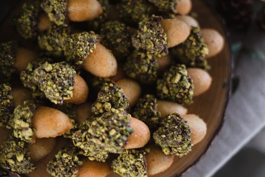 Small elongated pastries dipped in chopped pistachios on a wooden platter.