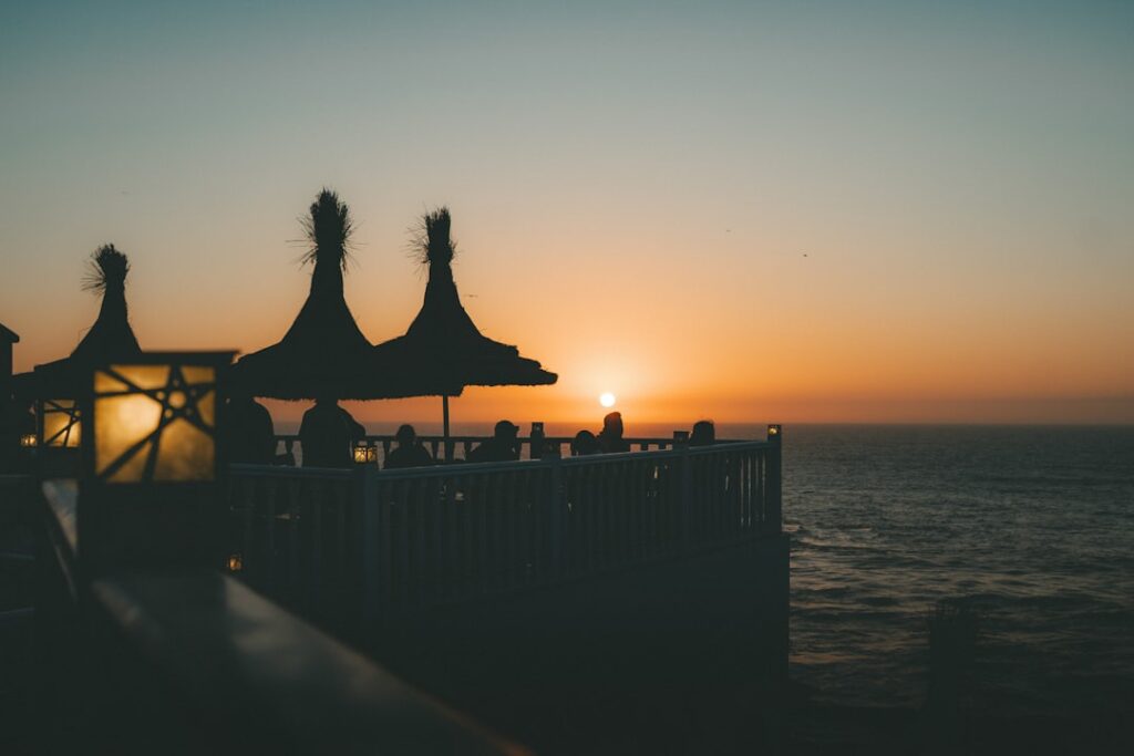 Seafront terrace in Catania with straw parasols silhouetted at sunset