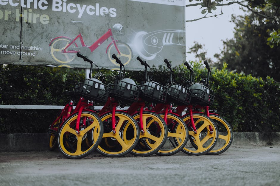 Red and yellow electric rental bicycles parked against advertising billboard