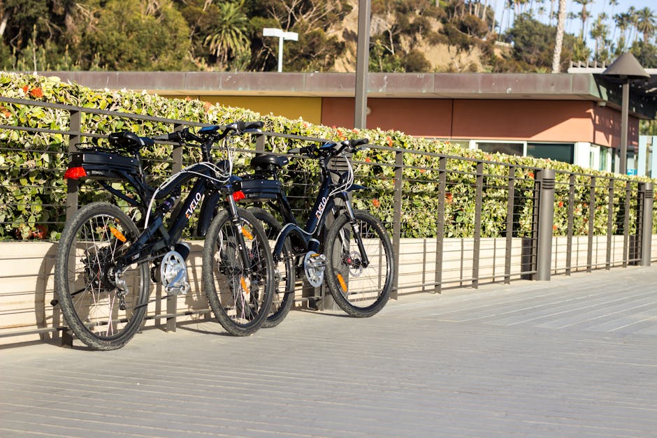 Three black electric bikes locked to railing on sunny promenade