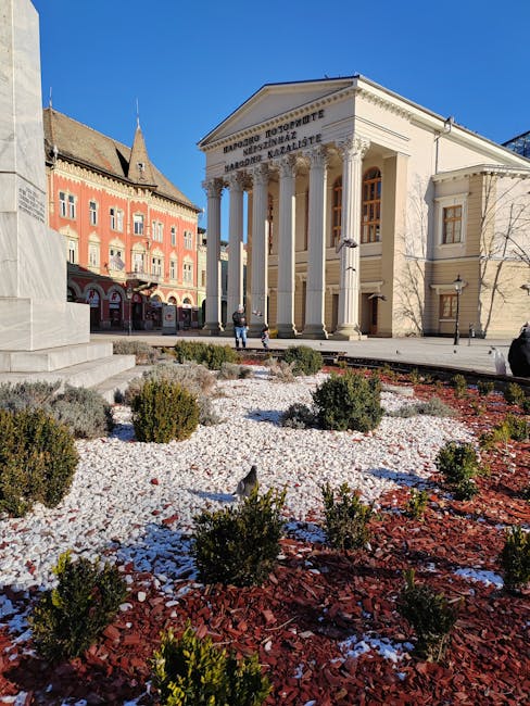 Neoklasyczny budynek teatralny z kolumnami i ozdobnym placem przed.