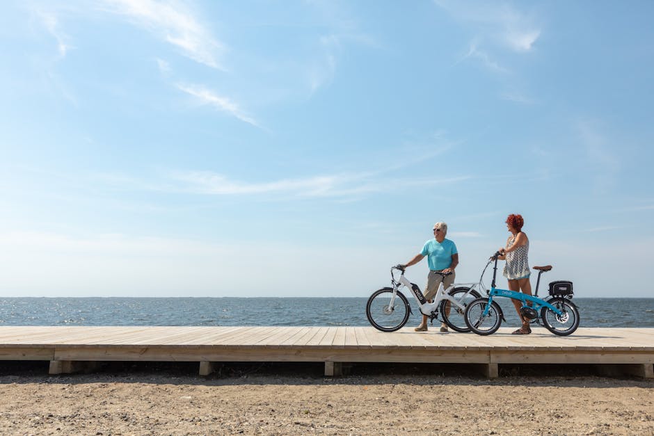 Two people with e-bikes standing on wooden boardwalk by the sea