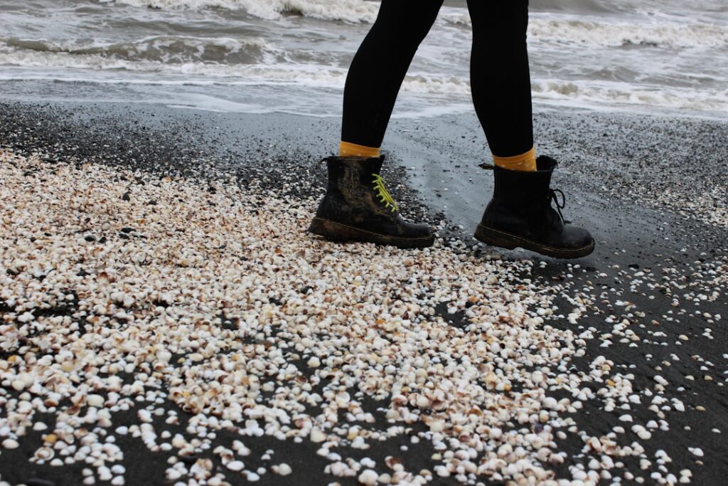 Bottes marchant sur sable noir jonché de coquillages près de Catane