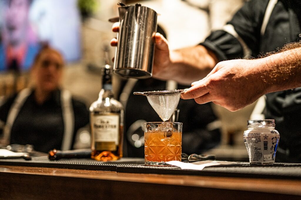 Bartender straining cocktail into glass at a dim bar in Catania.