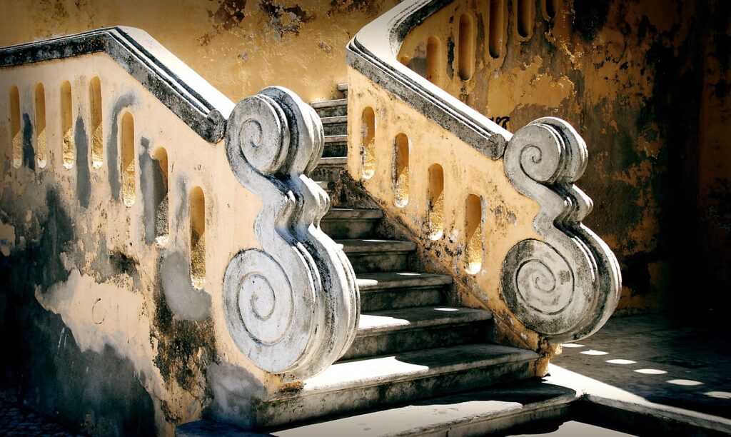 Zdobione skręcone balustrady i żółta odpadająca ściana przy schodach