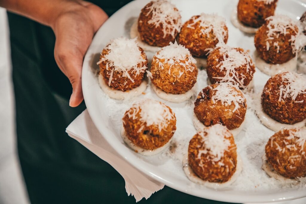Talerz z arancini posypanymi serem trzymany w dłoni w Katanii.