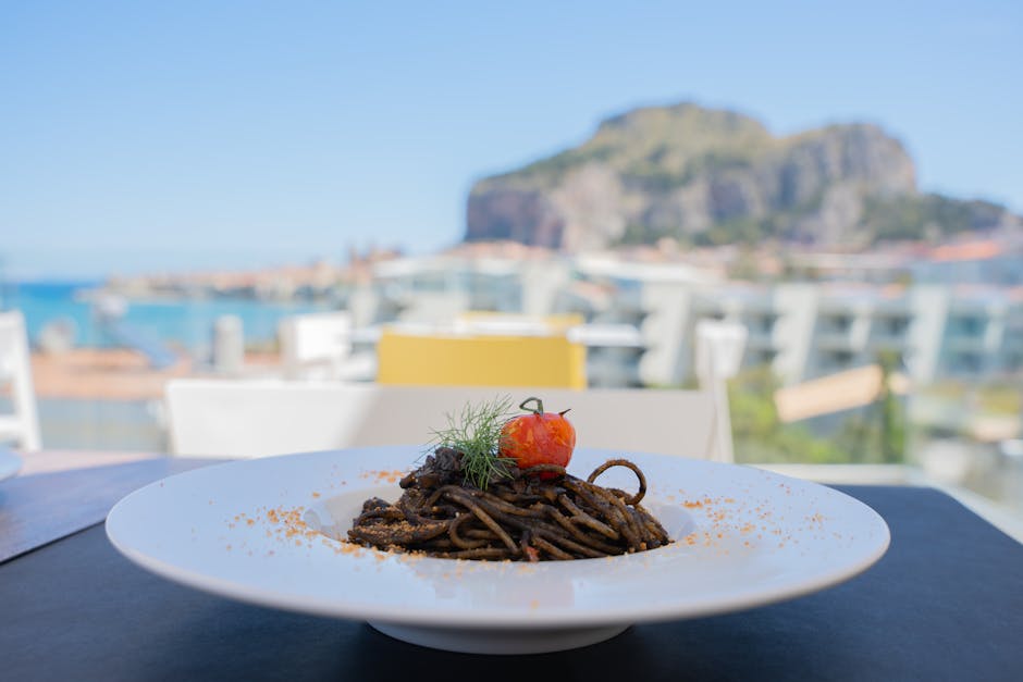 Squid-ink pasta garnished with tomato on a terrace overlooking Catania coast