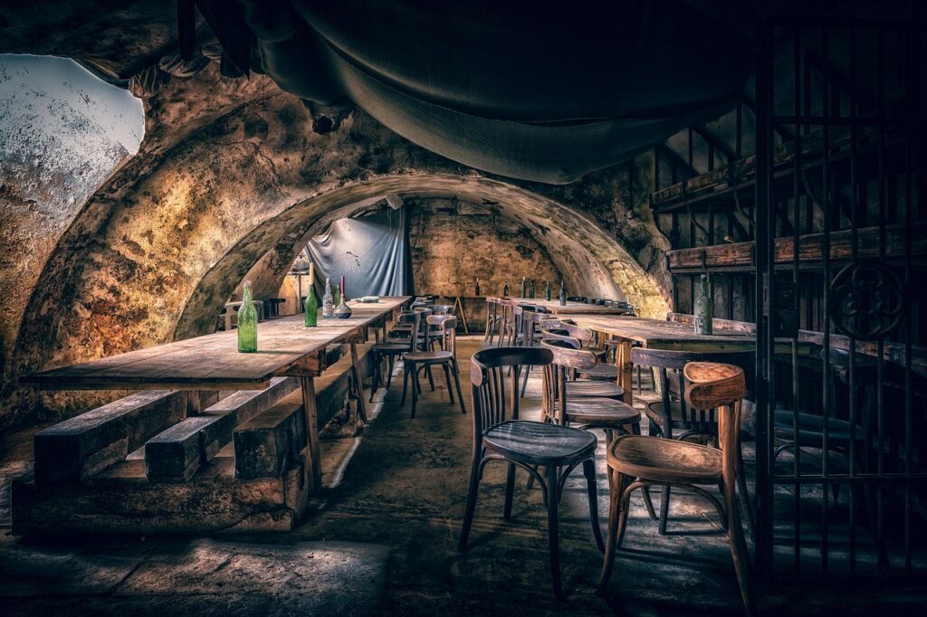 Gewölbter Kellerraum mit langen Holztischen und Flaschen in Catania.