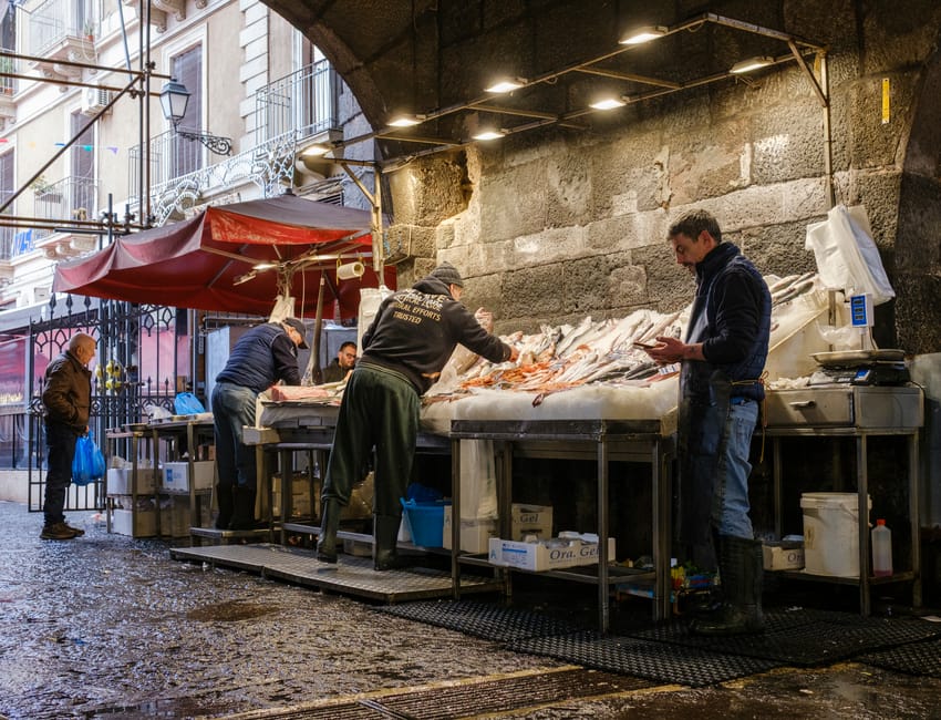 Vissstand onder boog in Catane markthal, verkopers sorteren verse vis