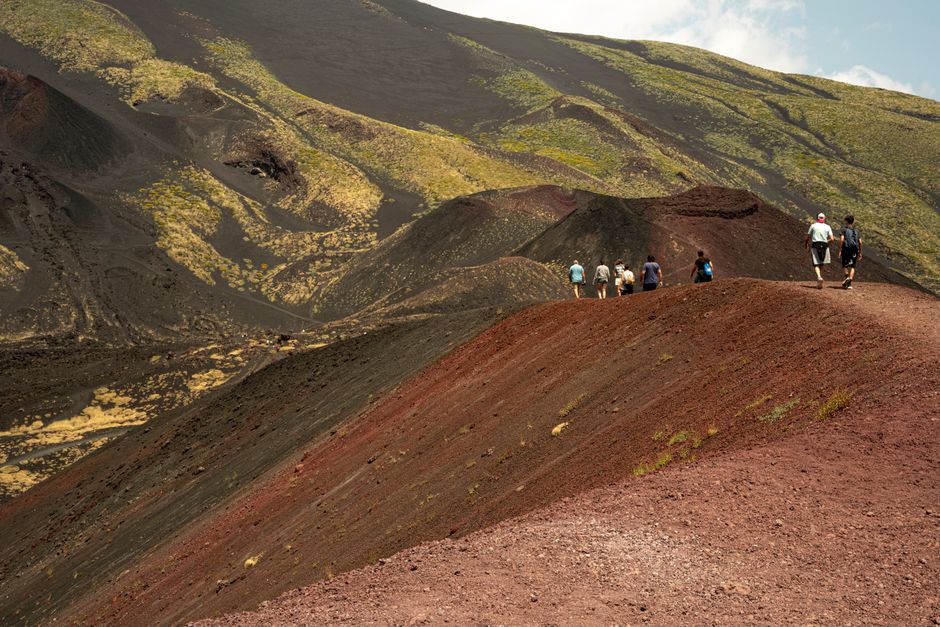 Randonneurs suivant une crête de cendres volcaniques rouges sur l'Etna