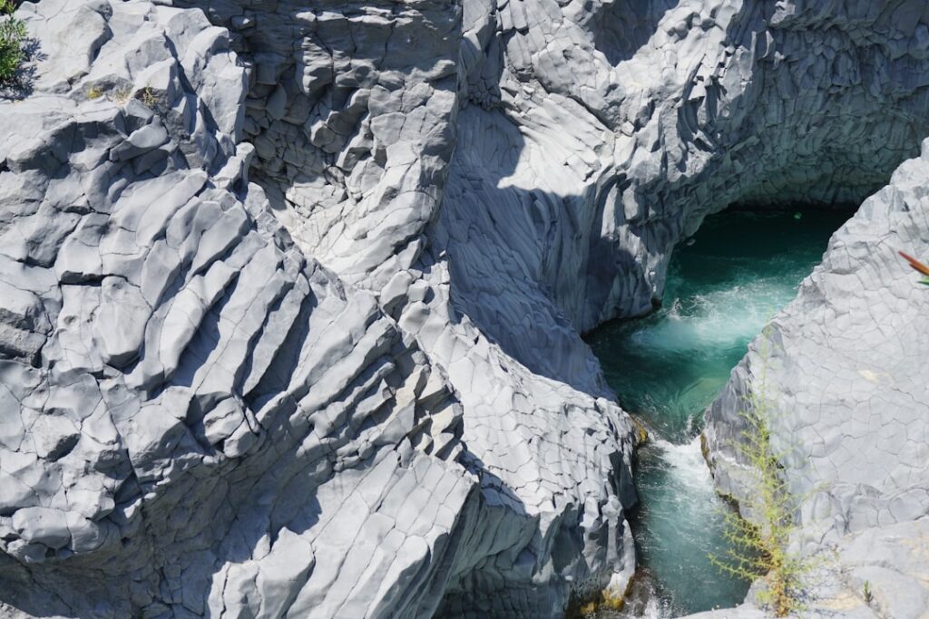 Gorges basaltique aux formes sculptées avec eau turquoise près de Catane