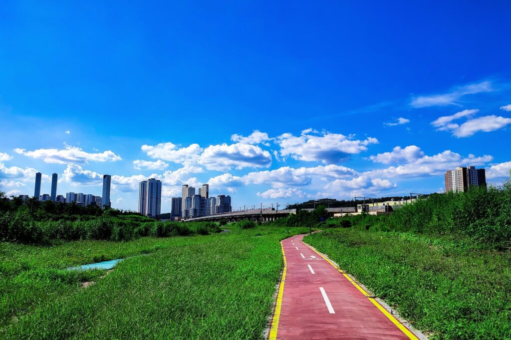 Piste cyclable rouge traversant une prairie vers une ligne d'horizon urbaine