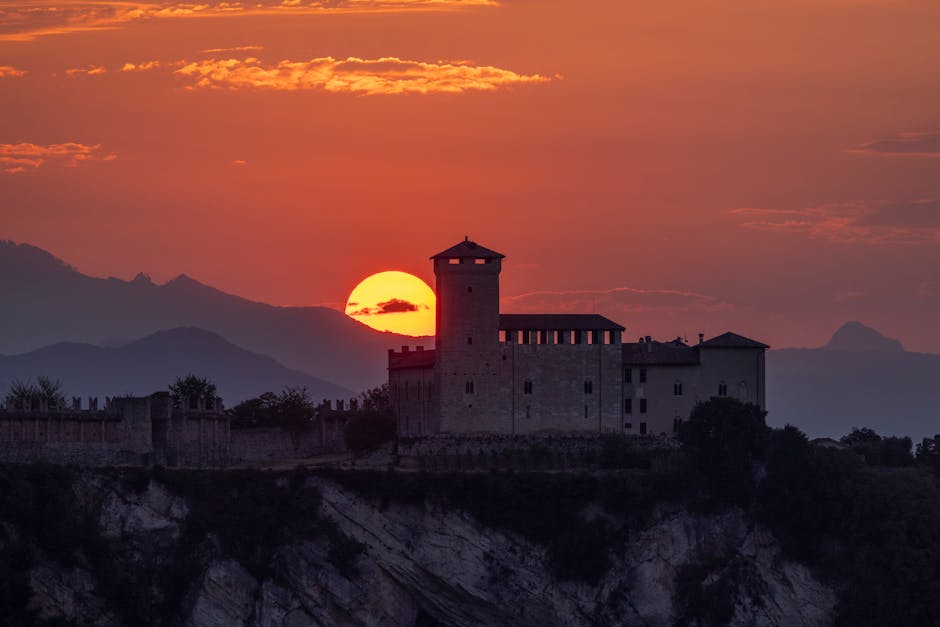 Burg auf steiler Klippe, Sonne sinkt hinter Bergen im Piemont.