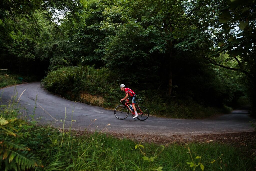 Fietser beklimt kronkelende bosweg, groene bomen langs route in Piémont