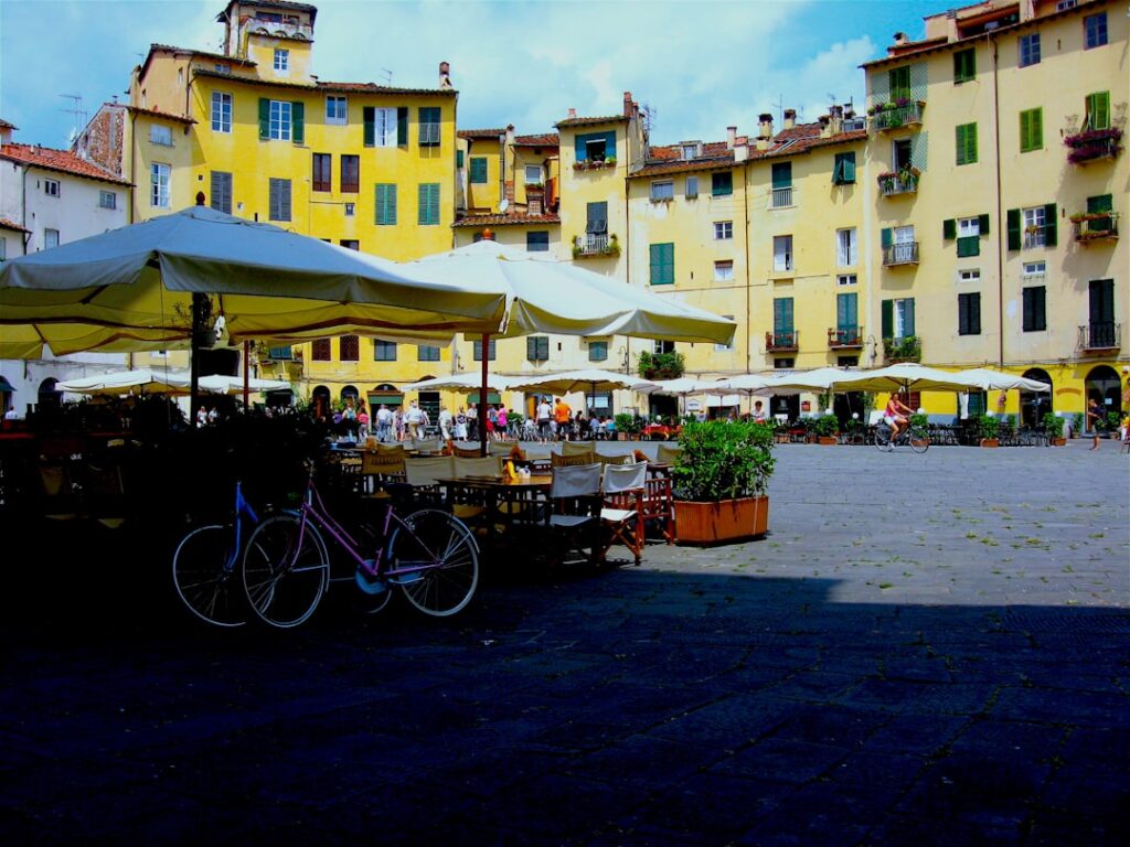 Piazza con tavolini all'aperto, ombrelloni bianchi e biciclette parcheggiate