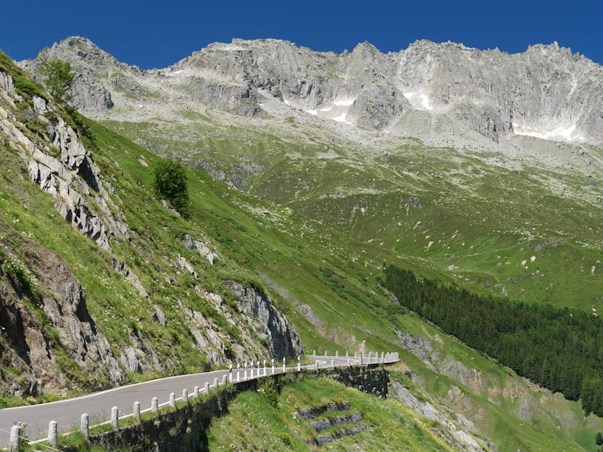 Serpentinenstraße entlang felsiger Hänge mit Alpenspitzern im Piemont