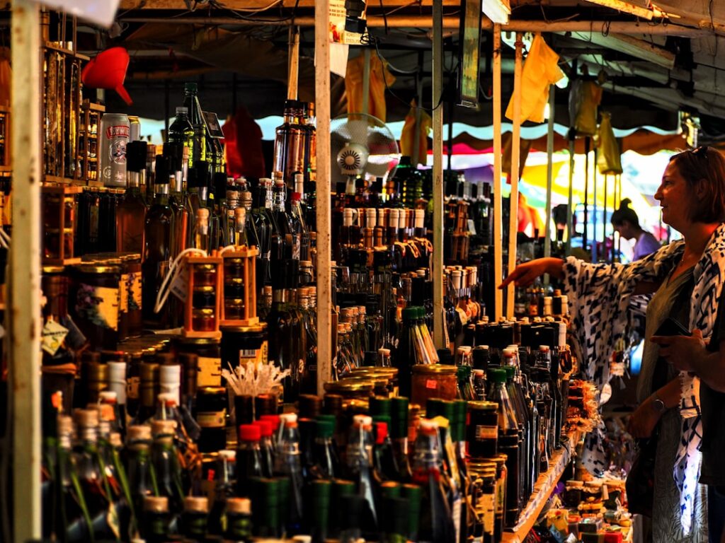 Marktstand mit Flaschen und Kundinnen auf einem Piemont‑Wochenmarkt