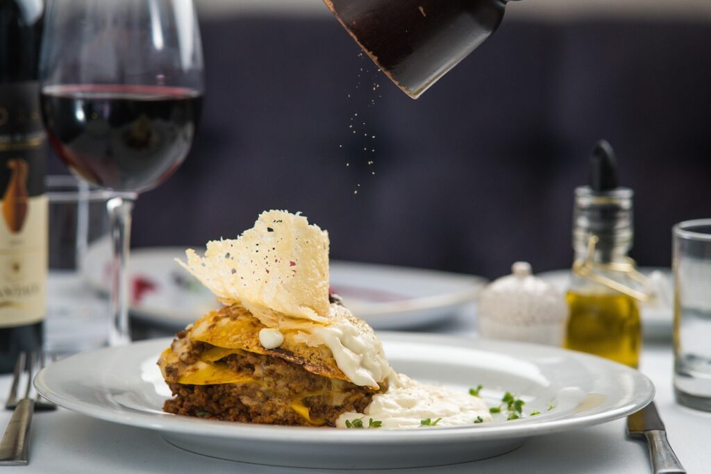 Close-up of layered lasagna being seasoned, paired with Piedmont red wine