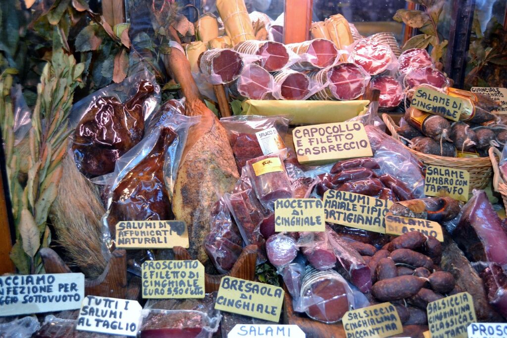 Vitrine mit luftgetrockneten Schinken, Salami und handschriftlichen Preisschildern in Piemont