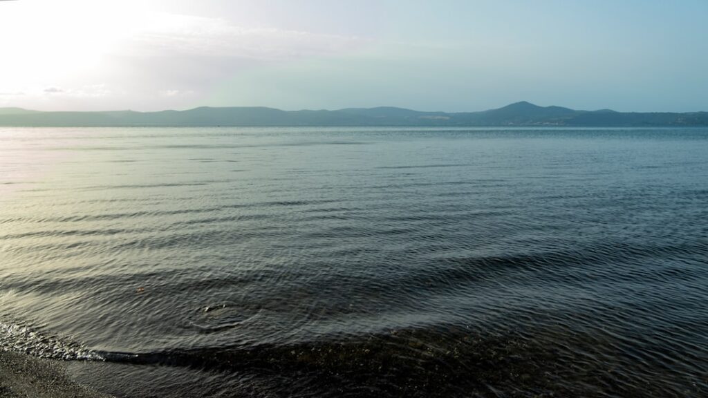 Riva tranquilla del Lago di Bracciano con onde leggere e colline lontane