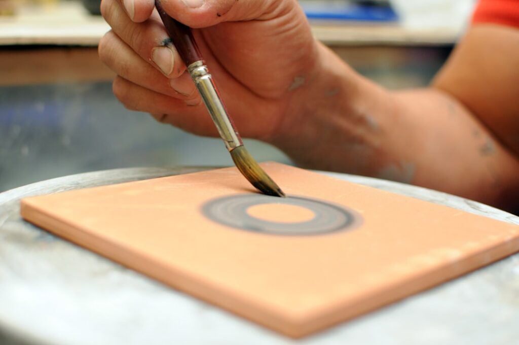 Artist painting concentric black rings on terracotta tile in Latium