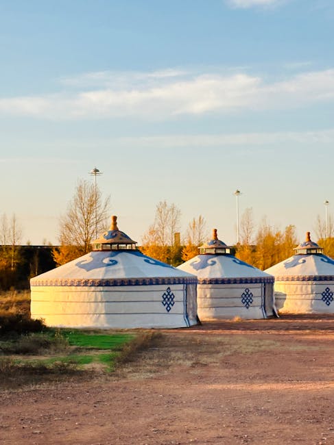 Three decorated white yurts pitched on open Latium field at dusk