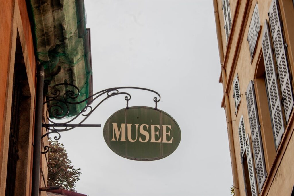 Een groen ovaal bord met 'MUSEE' hangt aan sierlijke ijzeren beugel in Latium.