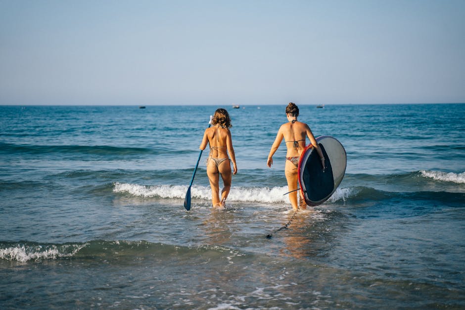 Zwei Frauen mit Paddleboard und Paddel waten ins Wasser von Lido di Ostia