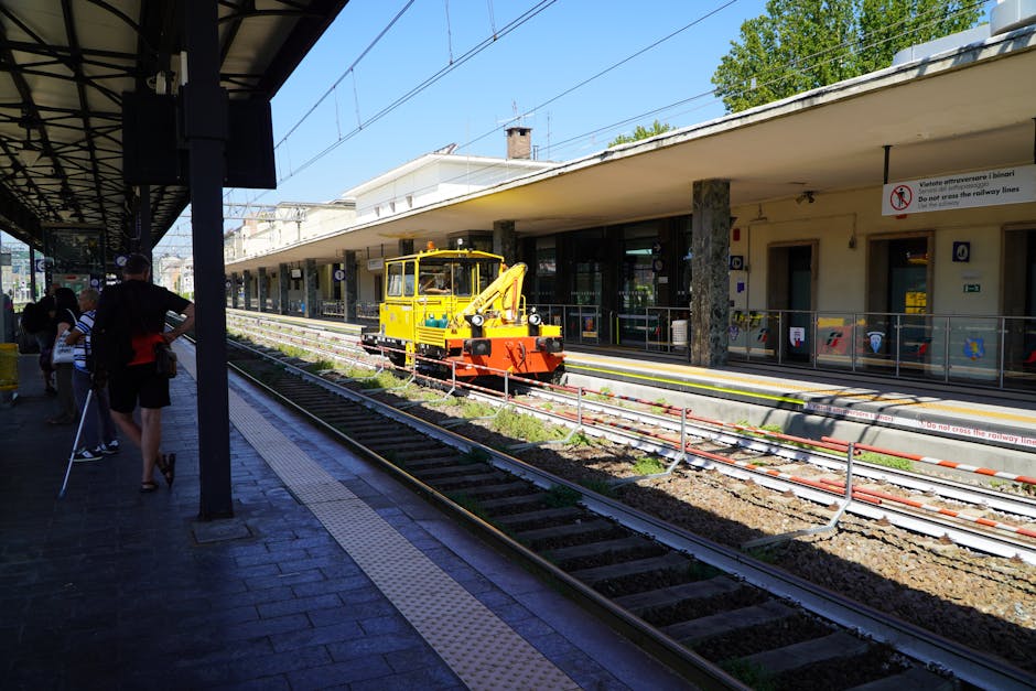 Gelbes Gleis-Wartungsfahrzeug auf Bahnsteig neben wartenden Reisenden