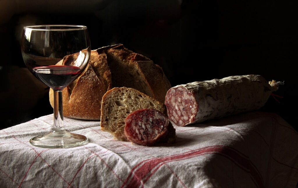 Brood, plakjes salami en glas rode wijn op tafellaken in Latium