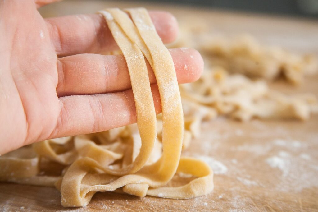 Hand holding fresh tagliatelle pasta strips on floured board in Latium