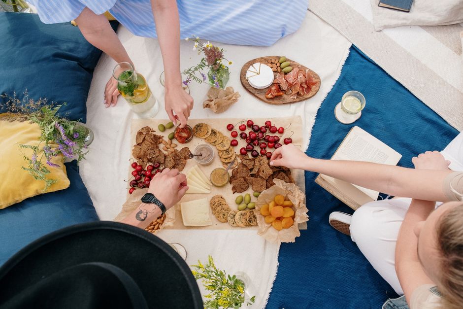 Picknickdecke mit Käse, Crackern, Oliven und Früchten, Hände greifen zu