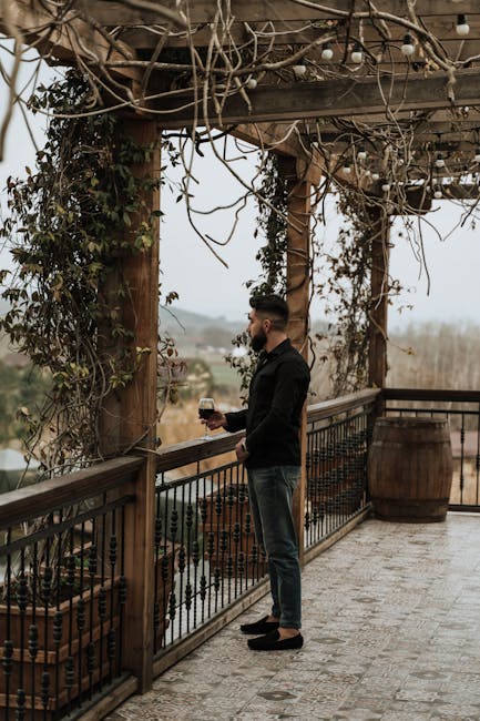 Man standing on vine-covered wooden terrace holding red wine, overlooking Latium countryside