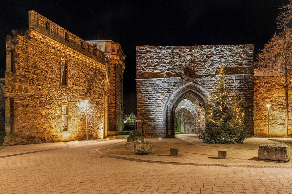 Verlichte stadspoort en muren bij nacht, kerstboom op plein in Perugia