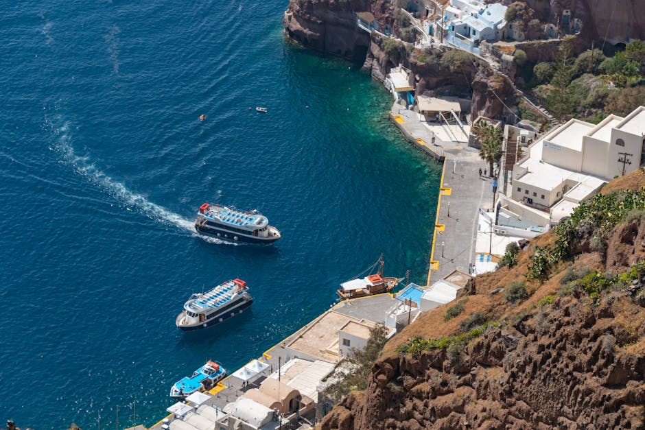 Dwa małe statki podpływają do przystani u podnóża Santorini