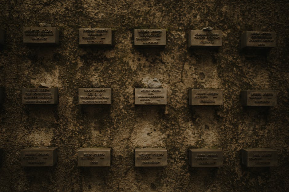Mur sombre percé de petites plaques nominatives disposées en grille