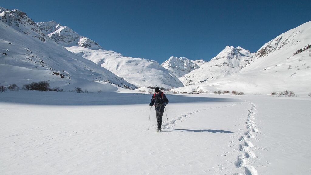 Randonneur en raquettes marchant sur un vaste plateau enneigé entouré de montagnes