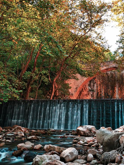 Waterval en stenen boogbrug tussen bosrijke oevers op Kreta