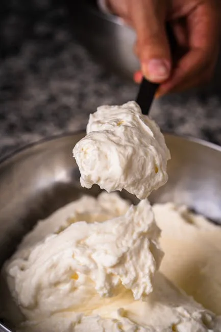 Cuiller soulevant une crème de fromage frais dans un bol métallique