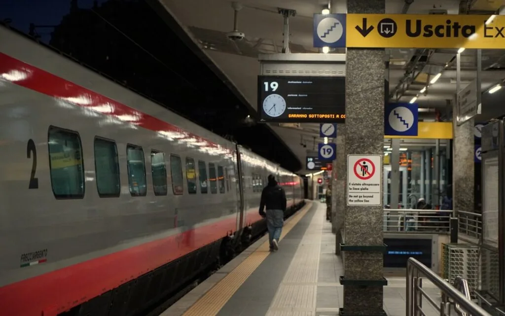 Quai de gare italien avec un train à grande vitesse et panneaux 'Uscita'