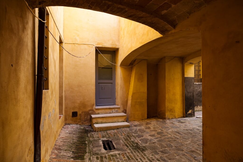 Sunny narrow courtyard with ochre walls and a blue door in Siena