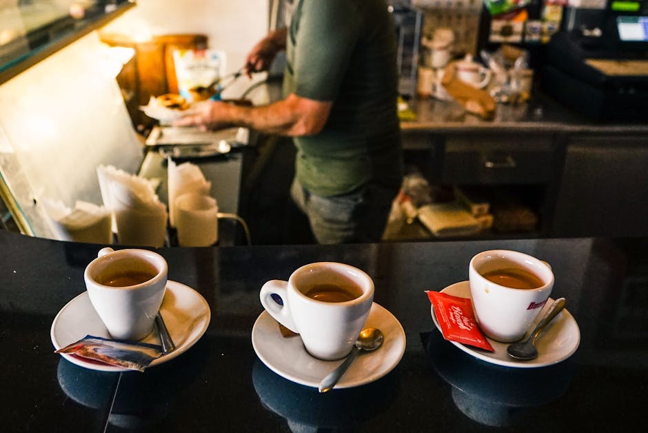 Three espresso cups on a Siena cafe counter, barista preparing drinks behind