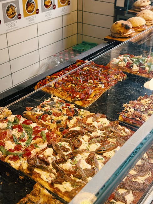 Assorted rectangular pizza slices displayed behind glass at Siena bakery counter